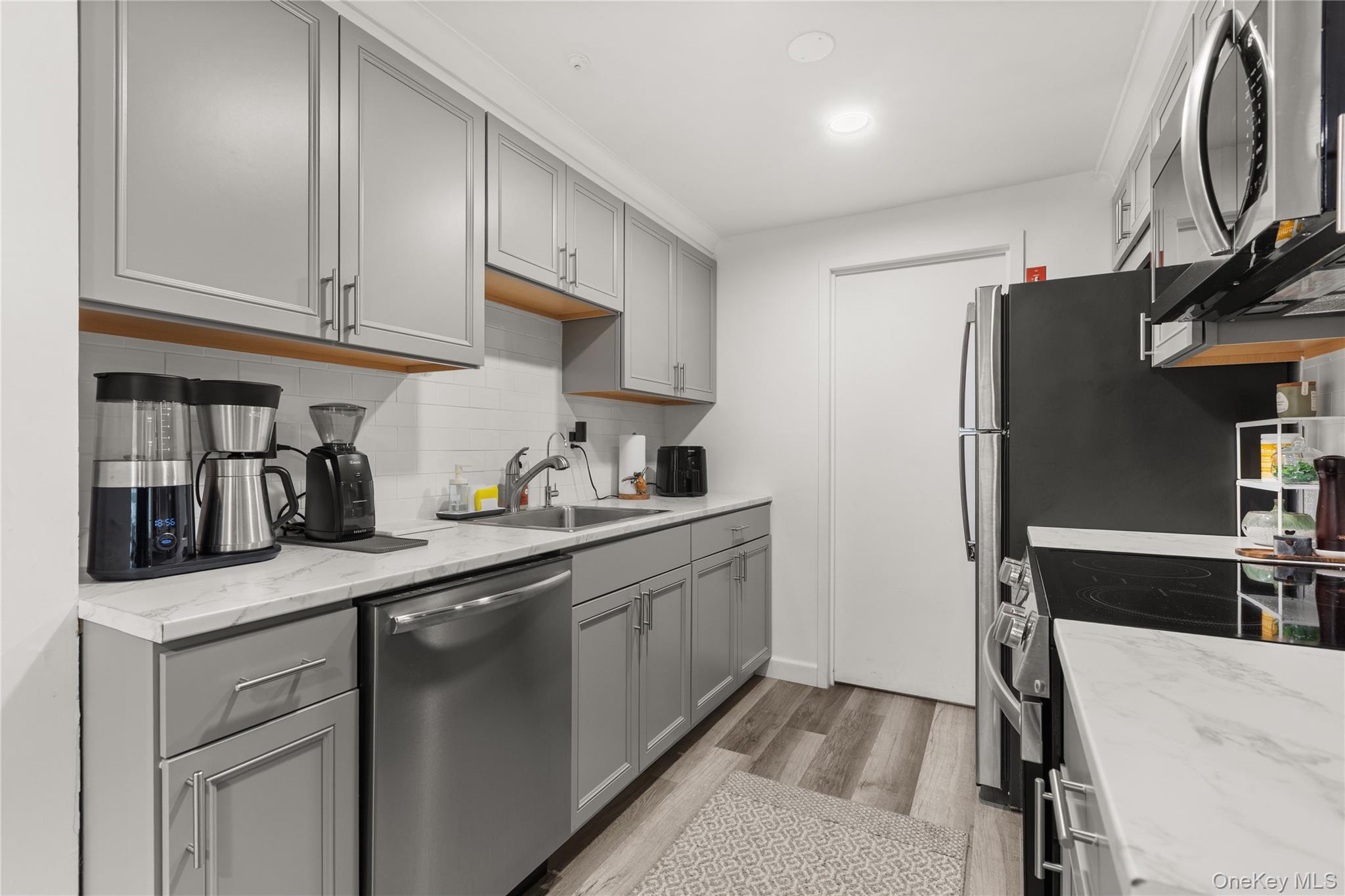 87 Birchwood Road Medford, NY 11763 - Photo 6 of 21 Kitchen with gray cabinets, stainless steel appliances, light wood-style flooring, backsplash, and light stone countertops