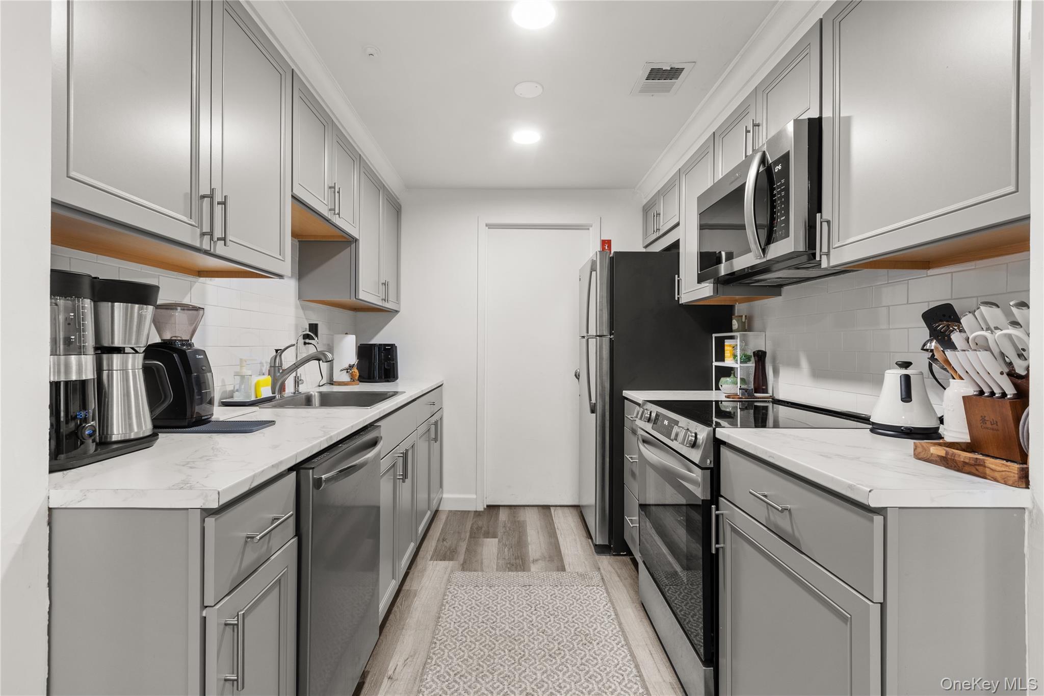 87 Birchwood Road Medford, NY 11763 - Photo 8 of 21 Kitchen with gray cabinetry, stainless steel appliances, light wood-type flooring, and decorative backsplash