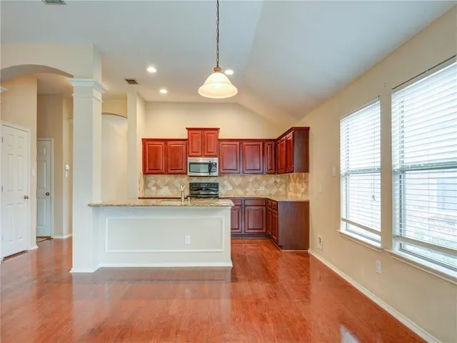 a open kitchen with stainless steel appliances granite countertop a stove a sink dishwasher a refrigerator and a fireplace with wooden floor