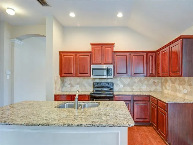 a kitchen with kitchen island granite countertop a sink a stove and a wooden cabinets