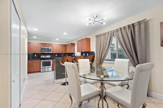 a kitchen with stainless steel appliances kitchen island granite countertop a refrigerator a stove a microwave oven a dining table and chairs with wooden floor