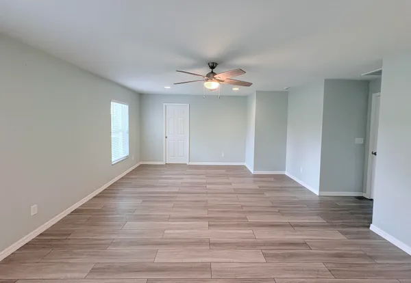 a view of an empty room with wooden floor and a ceiling fan