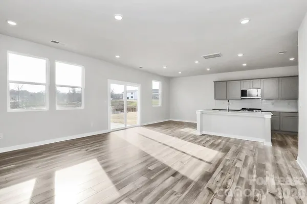 a large white kitchen with kitchen island a sink wooden floor and a large window