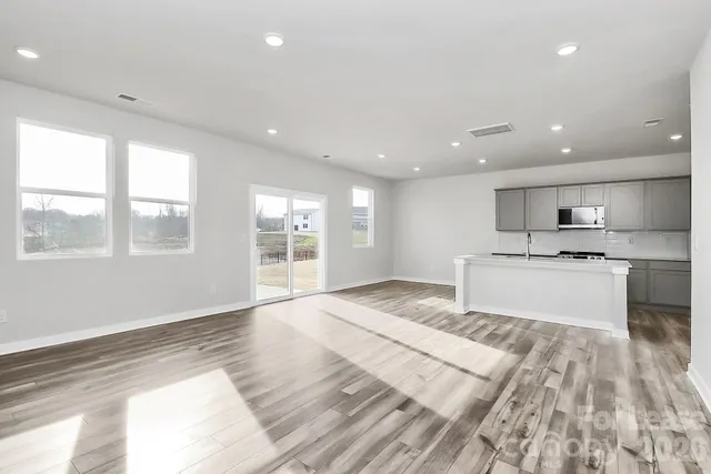 a large white kitchen with kitchen island a sink wooden floor and a large window