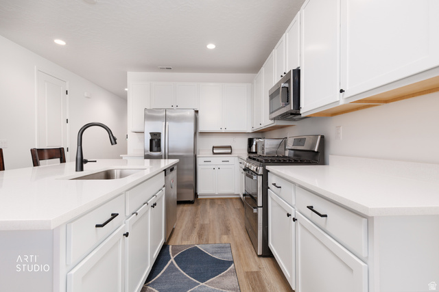 540 Lefty Lane Tooele, UT 84074 - Photo 7 of 48 Kitchen with stainless steel appliances, a center island with sink, light wood-style floors, recessed lighting, and white cabinets
