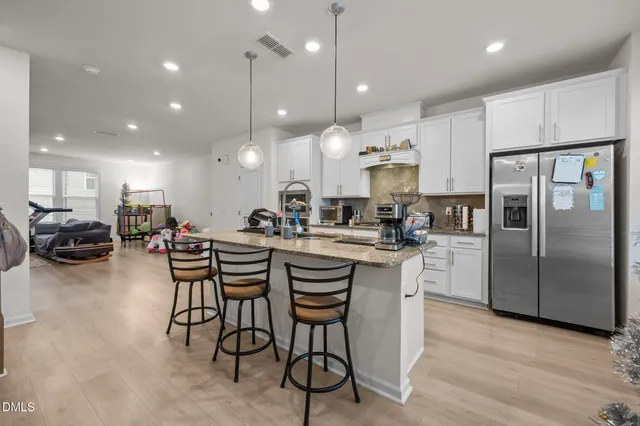 a kitchen with stainless steel appliances kitchen island granite countertop a dining table chairs refrigerator and microwave