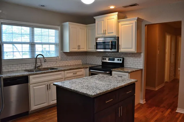 a kitchen with stainless steel appliances granite countertop a stove a sink dishwasher a refrigerator and a microwave oven with wooden floor