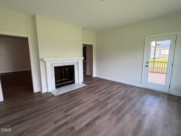 a view of an empty room with wooden floor fireplace and a window