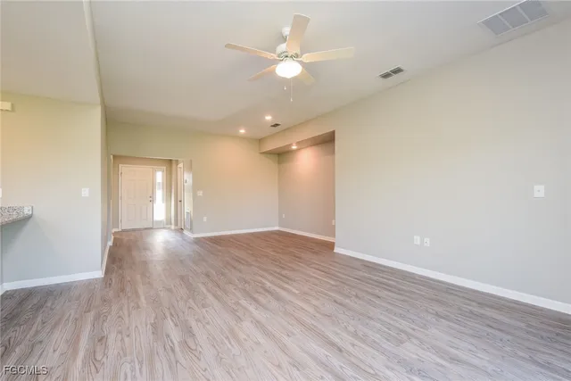 a view of an empty room with wooden floor and a ceiling fan