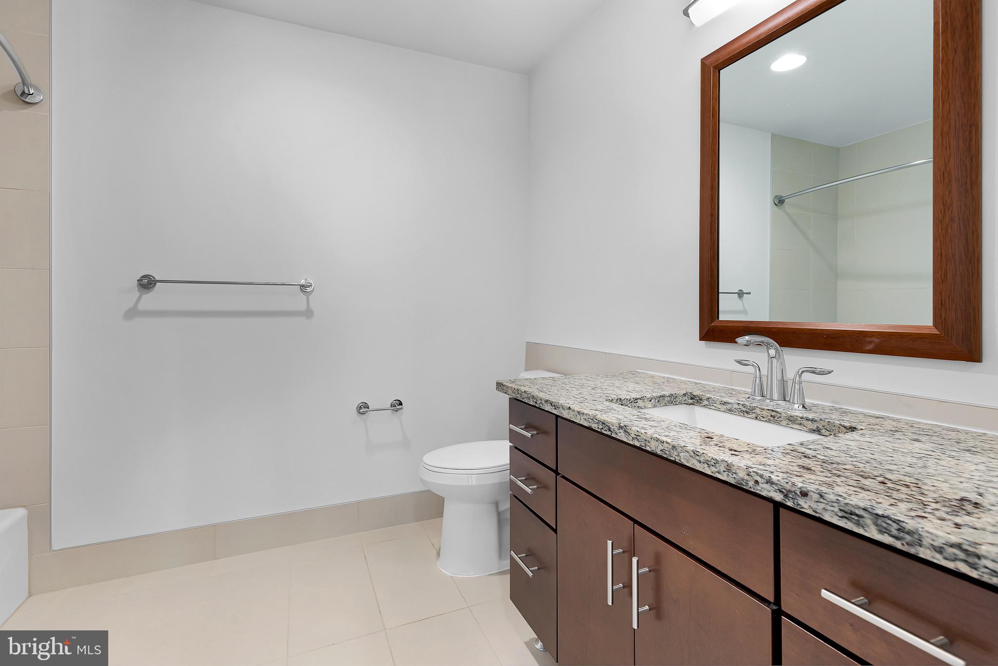 880 New Jersey Avenue Southeast, Unit STUDIO Washington, DC 20003 - Photo 4 of 24 a bathroom with a granite countertop sink a toilet and mirror