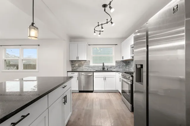 a kitchen with stainless steel appliances granite countertop a refrigerator a sink dishwasher a stove and white cabinets with wooden floor