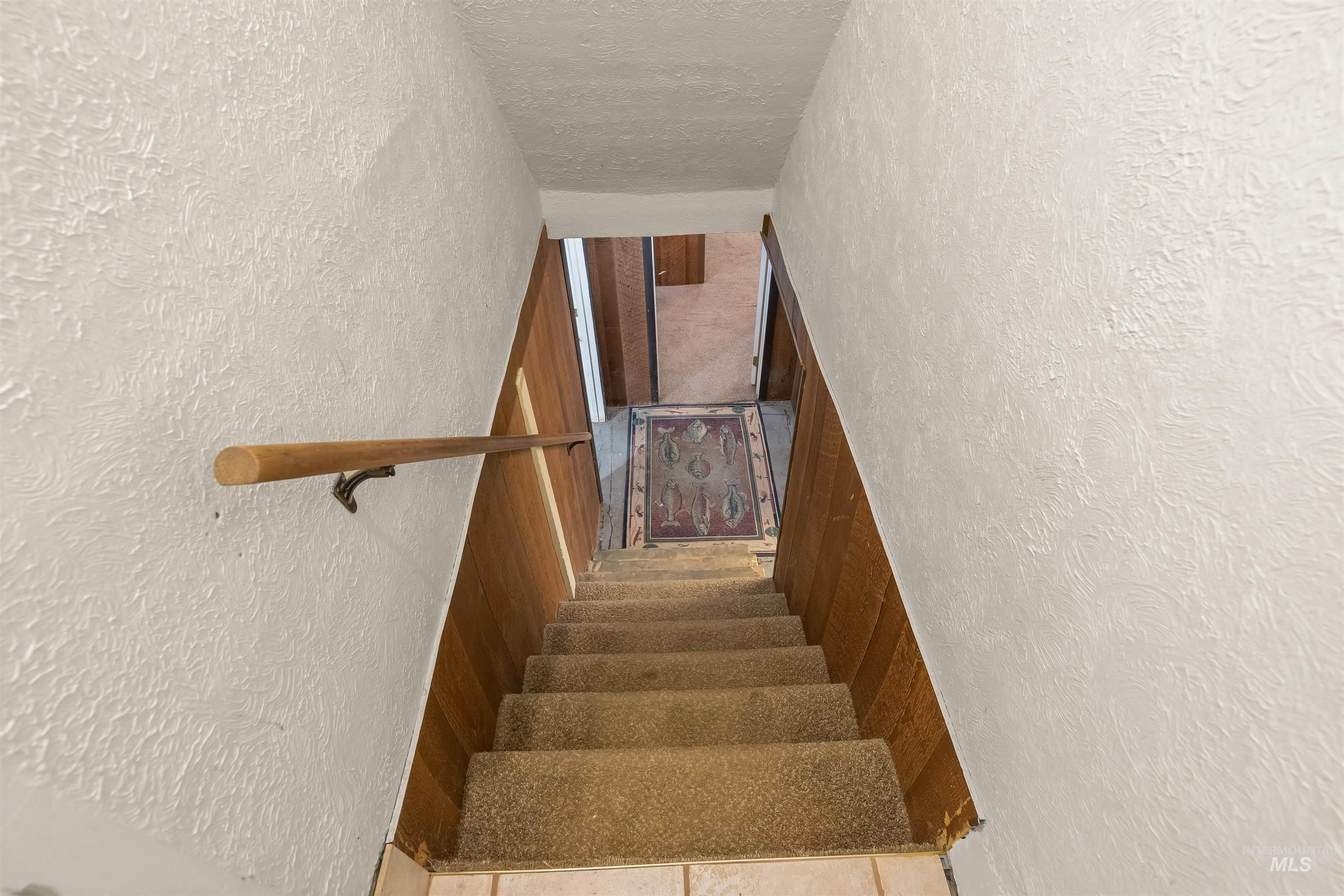 924 N Street Lewiston, ID 83501 - Photo 29 of 46 Staircase featuring wood-finish paneling, textured white walls, a wood handrail, and carpeted treads