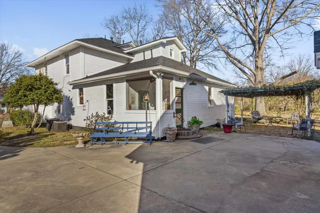 a view of a white house with large trees and wooden fence