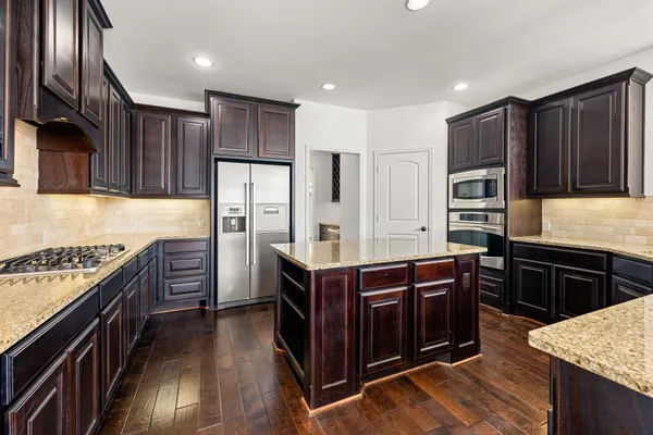 a kitchen with stainless steel appliances granite countertop a stove top oven a refrigerator and wooden cabinets