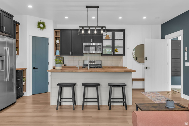 1766 West Tollgate Cyn Road Coalville, UT 84017 - Photo 30 of 59 Modern kitchen featuring black cabinetry, stainless steel appliances, a wood-finish countertop island, a geometric pendant light fixture, and light wood-finish flooring