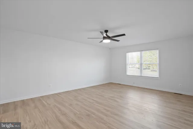 an empty room with wooden floor chandelier fan and windows
