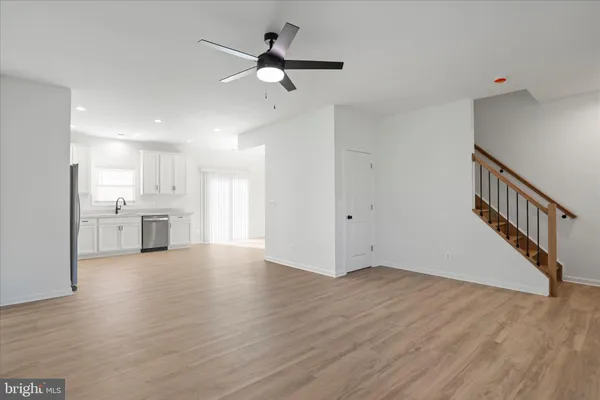 a view of an empty room with wooden floor and a kitchen