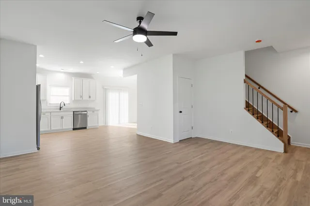 a view of an empty room with wooden floor and a kitchen