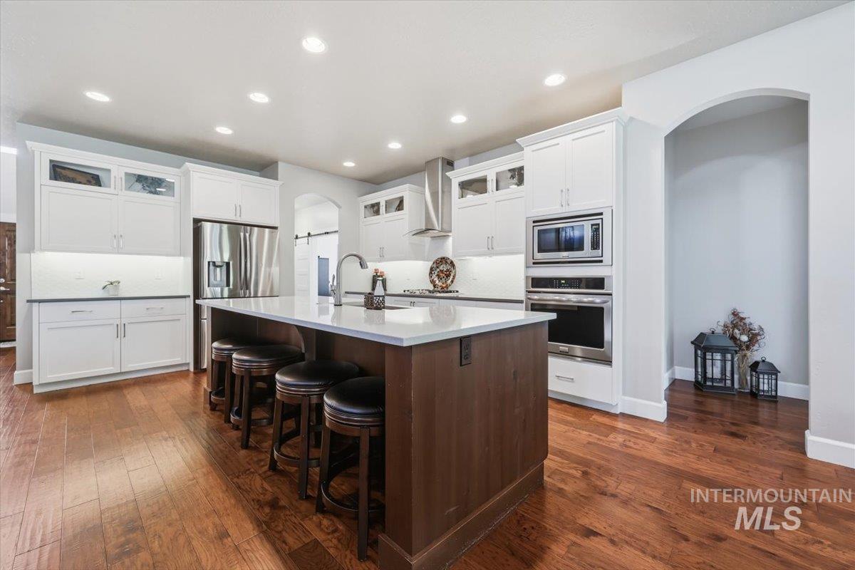 1303 West Brando Street Meridian, ID 83646 - Photo 11 of 49 Spacious kitchen featuring an expansive center island with seating, white cabinetry, stainless steel appliances including a built-in oven and microwave, and wood-finish flooring