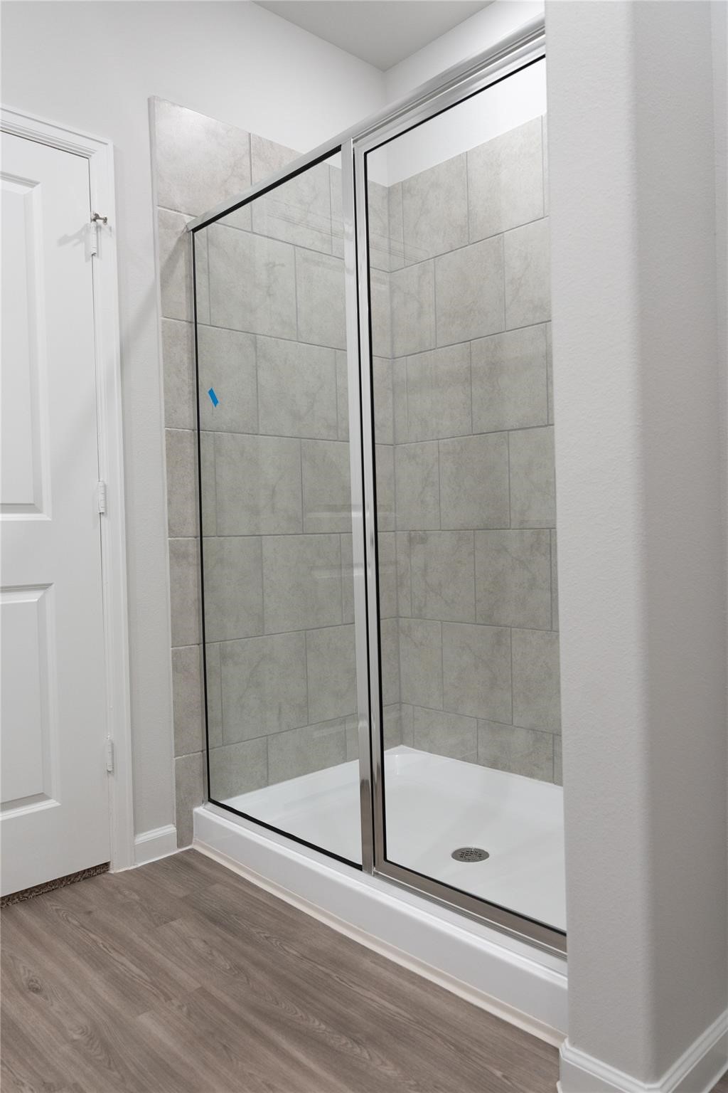 64 Valiant Ridge Trail Magnolia, TX 77354 - Photo 12 of 33 Primary bathroom with a glass-enclosed shower featuring light gray tile. The space has clean lines, a neutral color palette, and a wood-look floor, creating a contemporary feel.