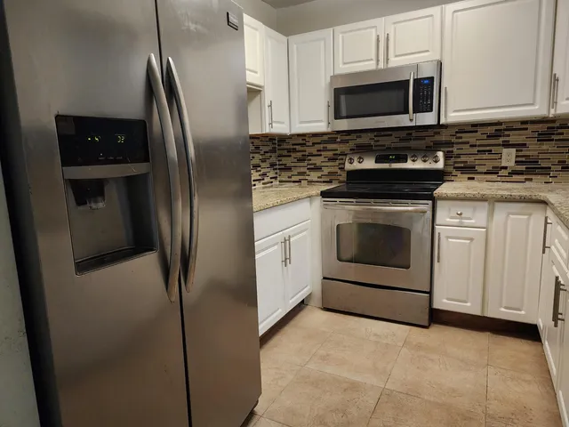 a kitchen with stainless steel appliances granite countertop a refrigerator stove a sink and white cabinets