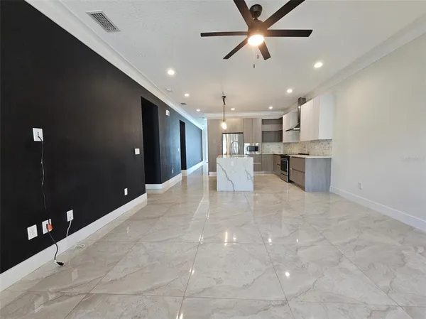a large white kitchen with a large counter top a refrigerator and a ceiling fan
