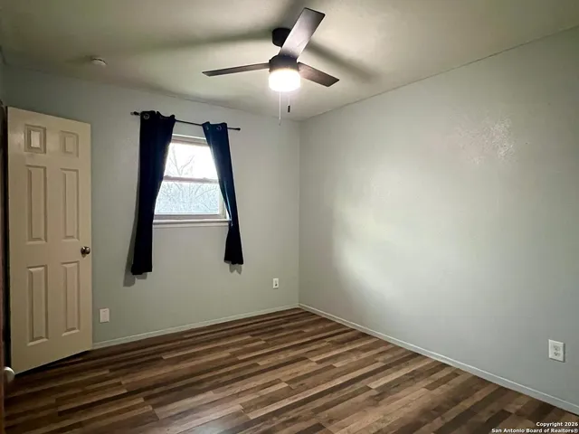 an empty room with wooden floor fan and windows
