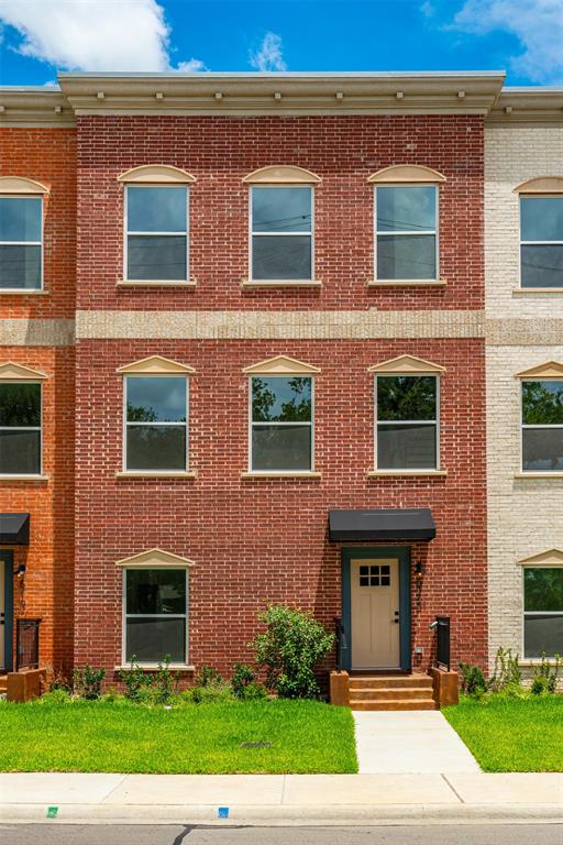 Three-story brick exterior featuring a cream-colored main entry door with a black awning, multiple windows with decorative sills, a manicured lawn, and a concrete pathway