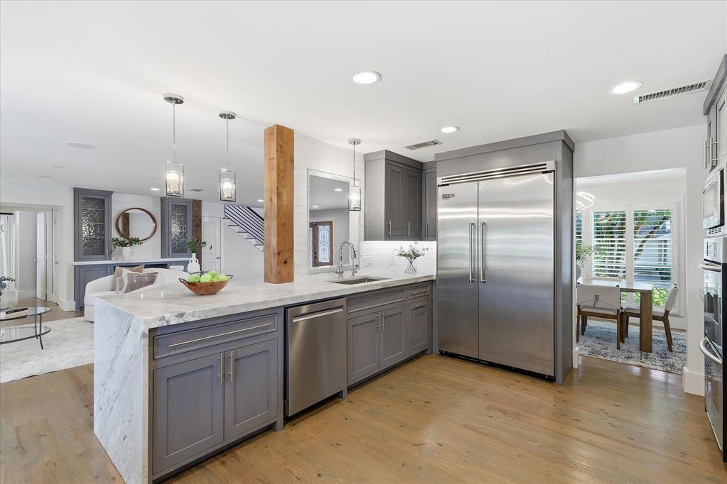 4310 Forest Bend Road Dallas, TX 75244 - Photo 11 of 40 Open concept kitchen featuring an oversized island with gray shaker cabinetry, stainless steel appliances, pendant lighting, and wood-finish flooring