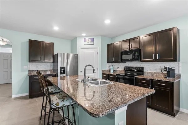 a kitchen with stainless steel appliances granite countertop a sink a stove a refrigerator cabinets and chairs