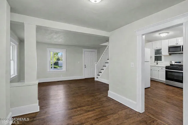 a view of empty room with kitchen and wooden floor