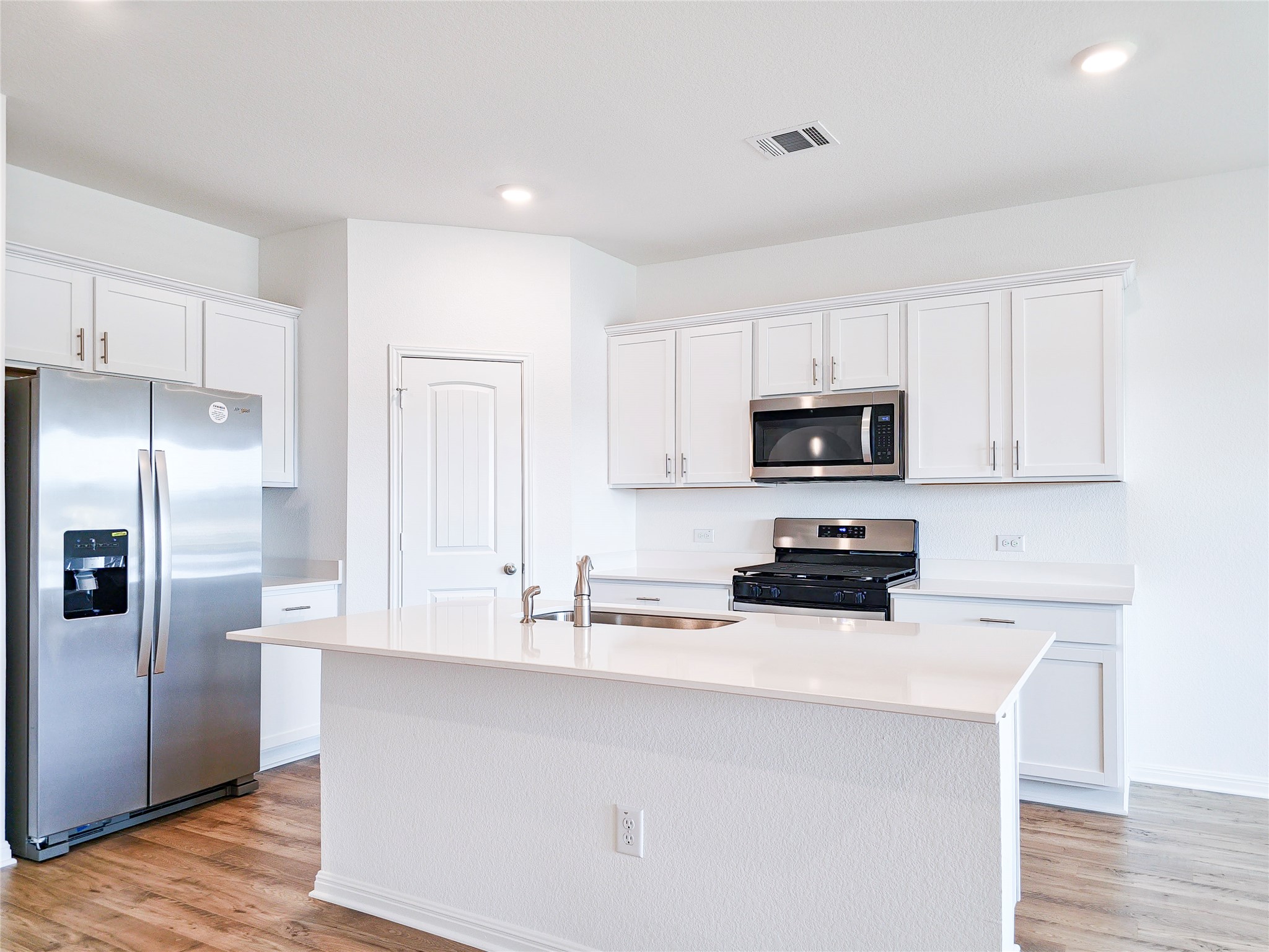 2313 March Hare Trace Leander, TX 78641 - Photo 13 of 30 Kitchen featuring stainless steel appliances, a center island with sink, white cabinets, light wood finished floors, and recessed lighting