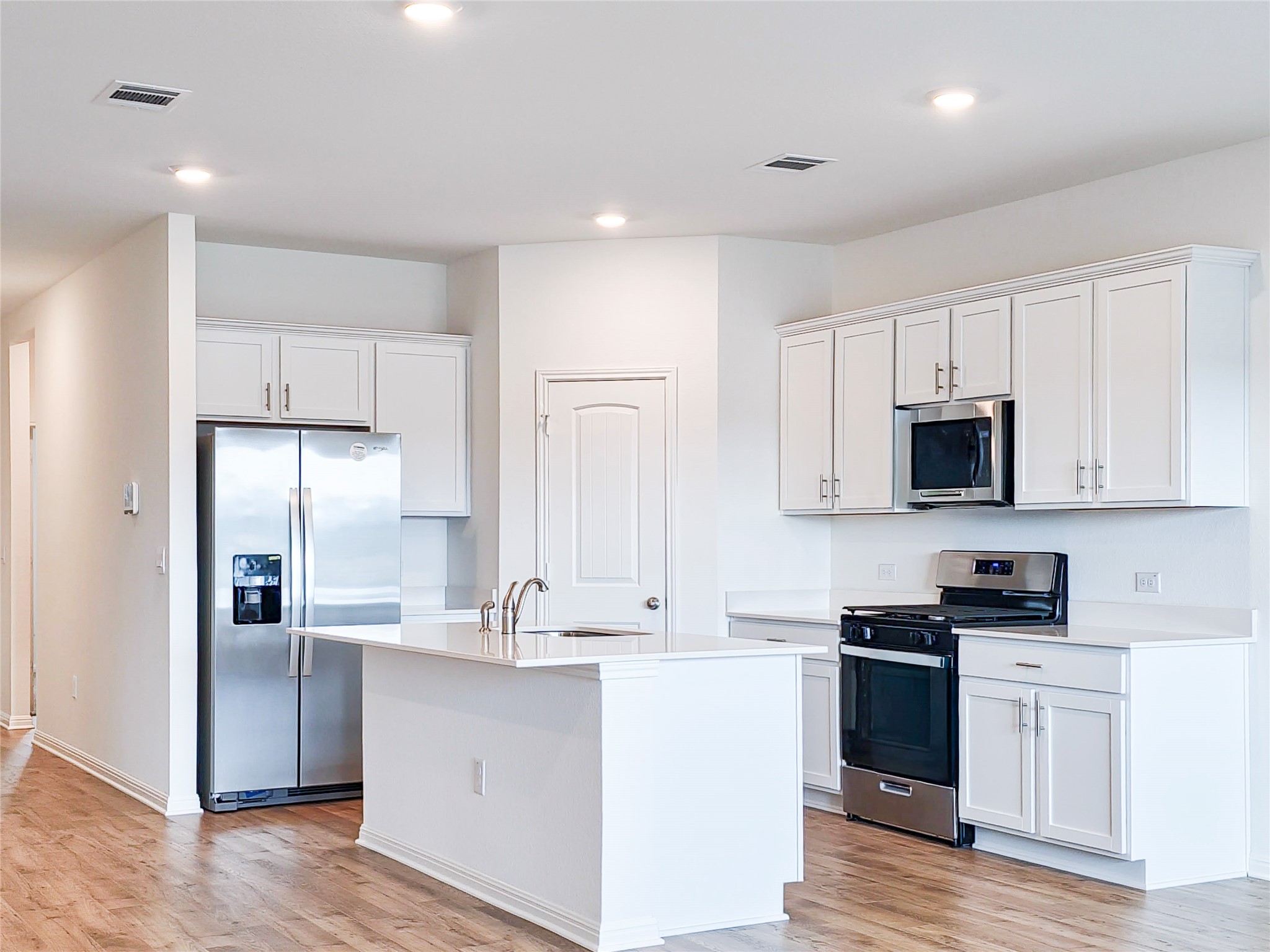 2313 March Hare Trace Leander, TX 78641 - Photo 8 of 30 Kitchen featuring stainless steel appliances, white cabinets, light wood-style flooring, a kitchen island with sink, and recessed lighting