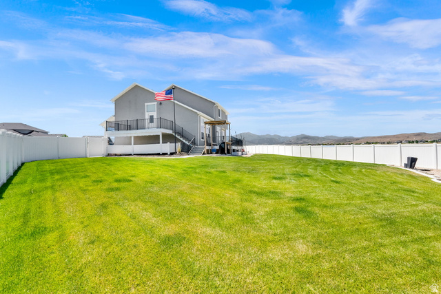 1857 Thunder Gulch Road Eagle Mountain, UT 84005 - Photo 40 of 50 Expansive backyard featuring a lush green lawn, full perimeter white vinyl fencing, and a two-story gray exterior home with a second-story deck and a ground-level covered patio