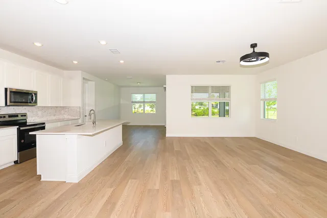 a large white kitchen with kitchen island a sink wooden floor and a living room view