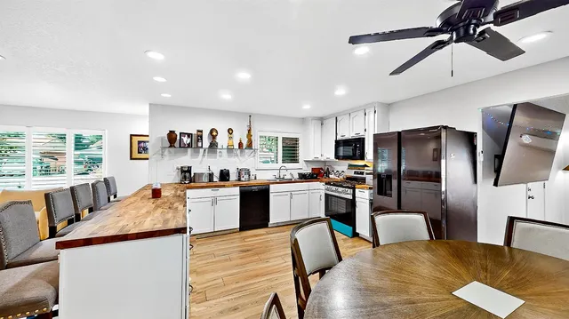 a kitchen with granite countertop stainless steel appliances a refrigerator a stove a sink a dining table and chairs with wooden floor