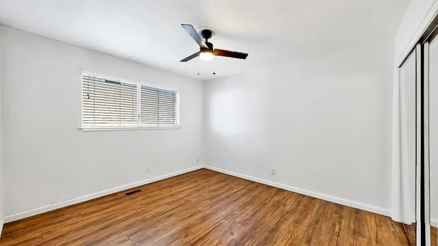 an empty room with wooden floor fan and windows