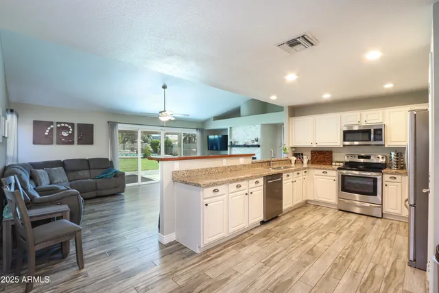 a large kitchen with stainless steel appliances granite countertop a stove top oven a sink dishwasher a dining table and chairs with wooden floor