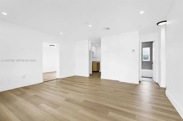 a view of an empty room with wooden floor and a kitchen