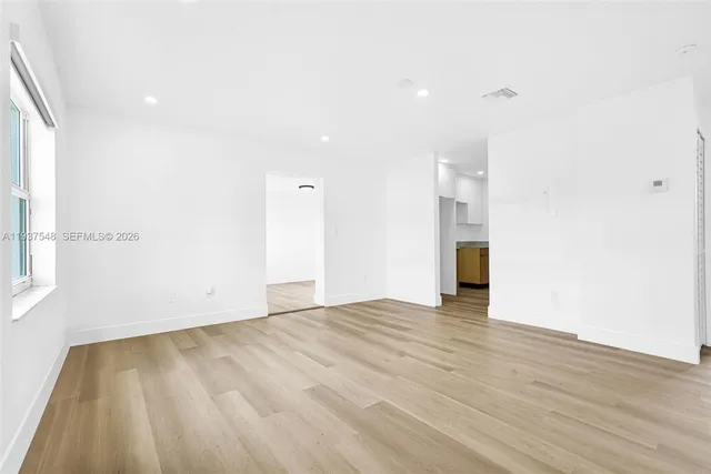 a view of an empty room with wooden floor and a window