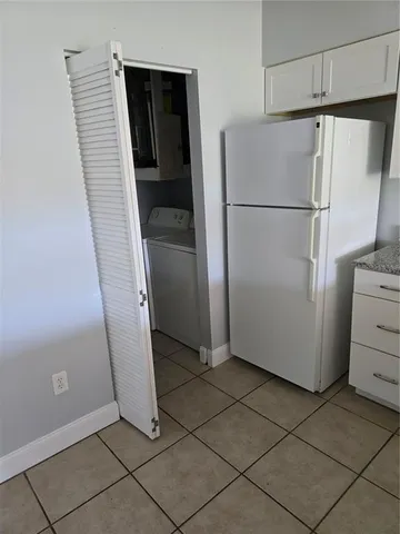 a view of a refrigerator in kitchen and an empty room with wooden floor