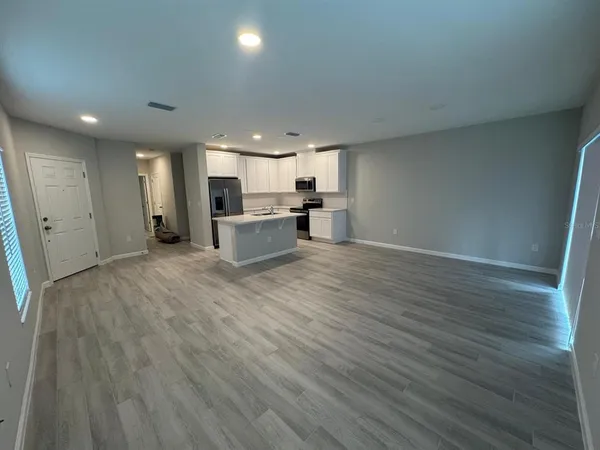 an empty room with wooden floor and a kitchen