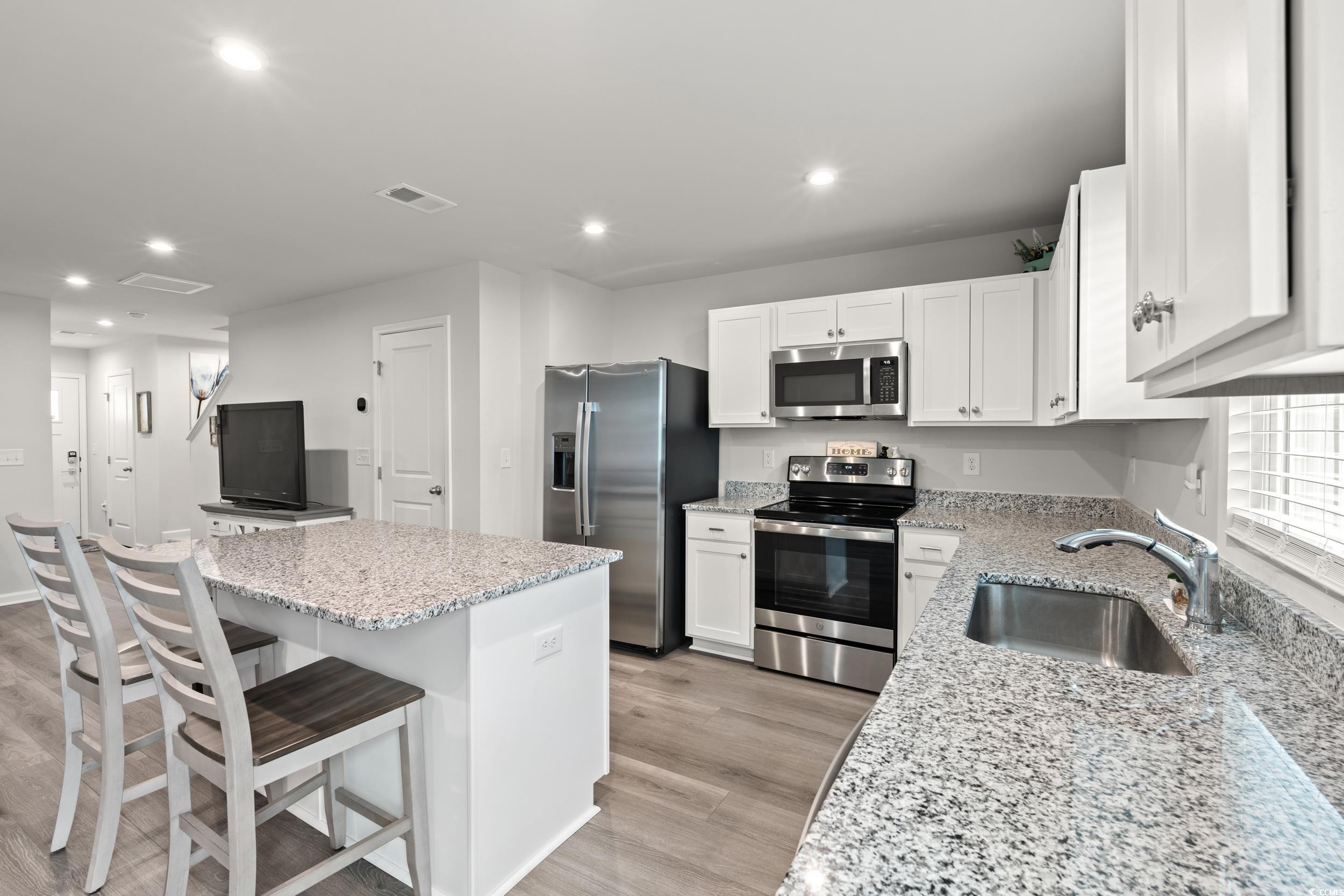 301 Granada Street, Unit D Myrtle Beach, SC 29579 - Photo 7 of 33 Kitchen with appliances with stainless steel finishes, white cabinetry, a kitchen breakfast bar, recessed lighting, and light stone counters