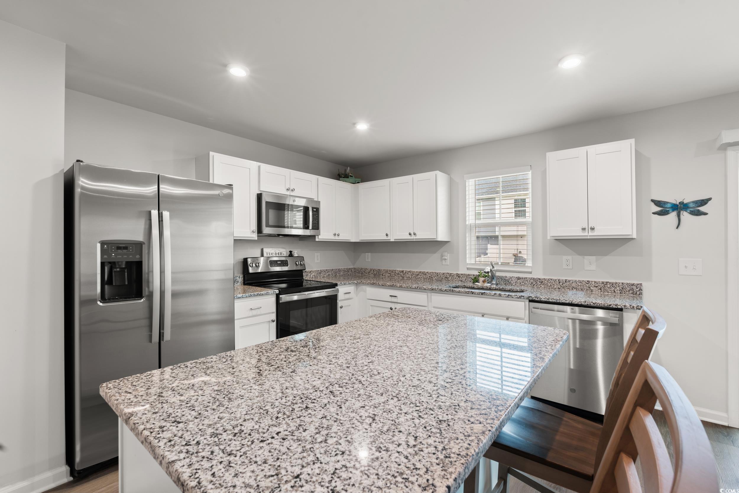 301 Granada Street, Unit D Myrtle Beach, SC 29579 - Photo 8 of 33 Kitchen featuring appliances with stainless steel finishes, light stone countertops, white cabinets, a kitchen island, and a breakfast bar