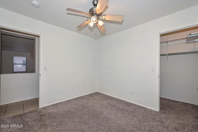 an empty room with a chandelier fan and windows