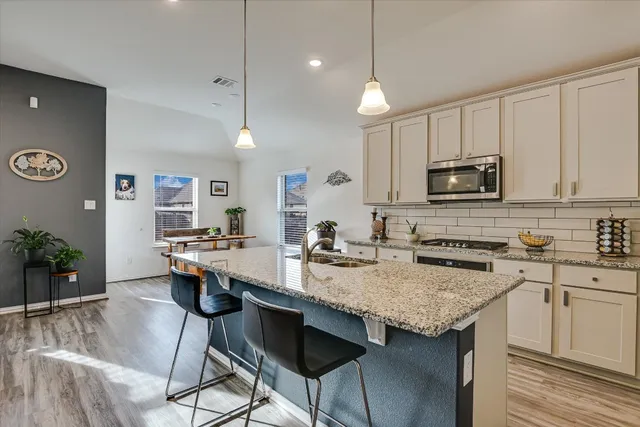 a kitchen with granite countertop a stove a sink a refrigerator and chairs