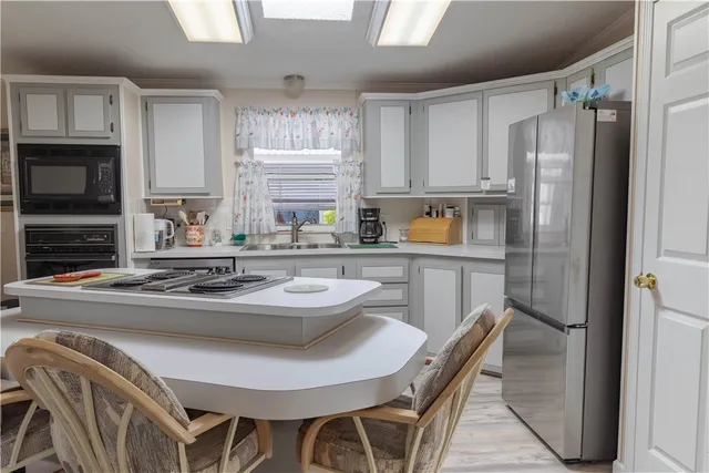 a kitchen with stainless steel appliances granite countertop a sink a stove a refrigerator cabinets and a dining table with wooden floor