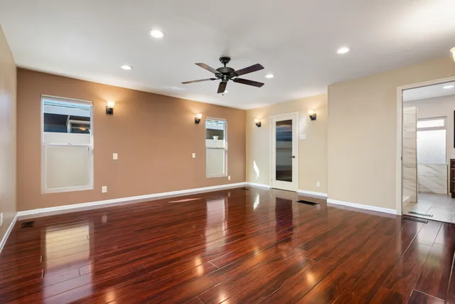 a view of an empty room with wooden floor and a ceiling fan