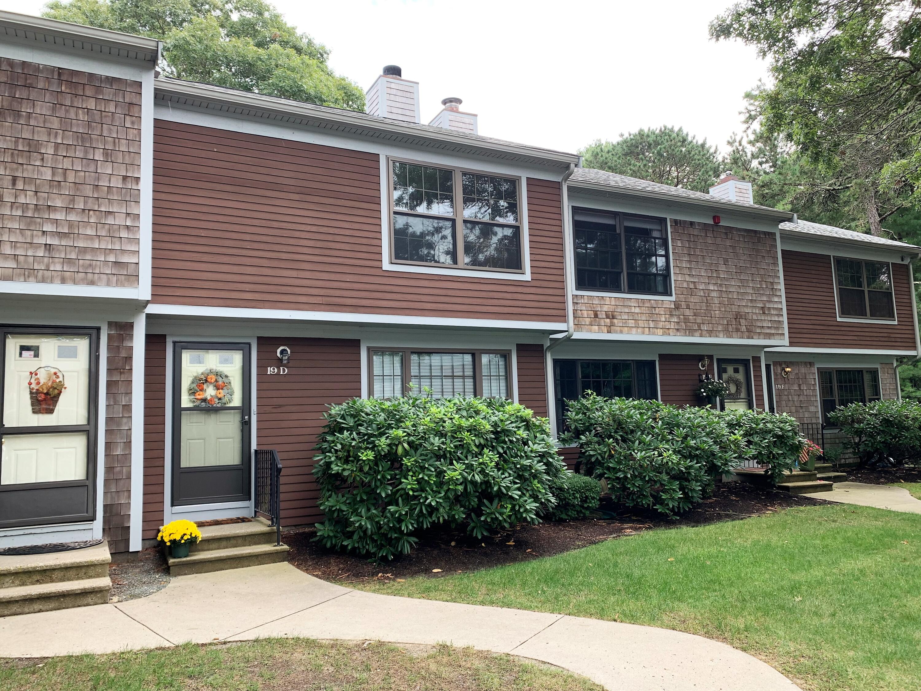 195 Falmouth Road, Unit 19D Mashpee, MA 02649 - Photo 1 of 17 a view of a brick house with a yard plants and large tree