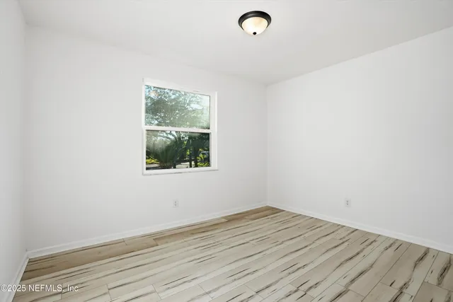 a view of an empty room with wooden floor and a bathroom